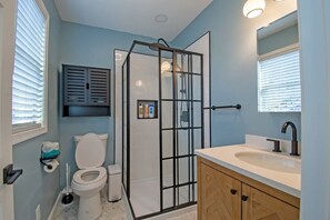 Ein Badezimmer mit Glasdusche, Toilette, Waschbecken mit Spiegel und Schrank.