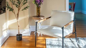 Ein modernes Wohnzimmer mit Holzboden, einem weißen Ledersessel, einer Topfpflanze und einer Vase mit Blumen.