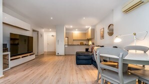 Un salon moderne doté d’un téléviseur à écran plat, d’une table à manger avec des chaises, d’un canapé et d’un coin cuisine à l’arrière-plan.