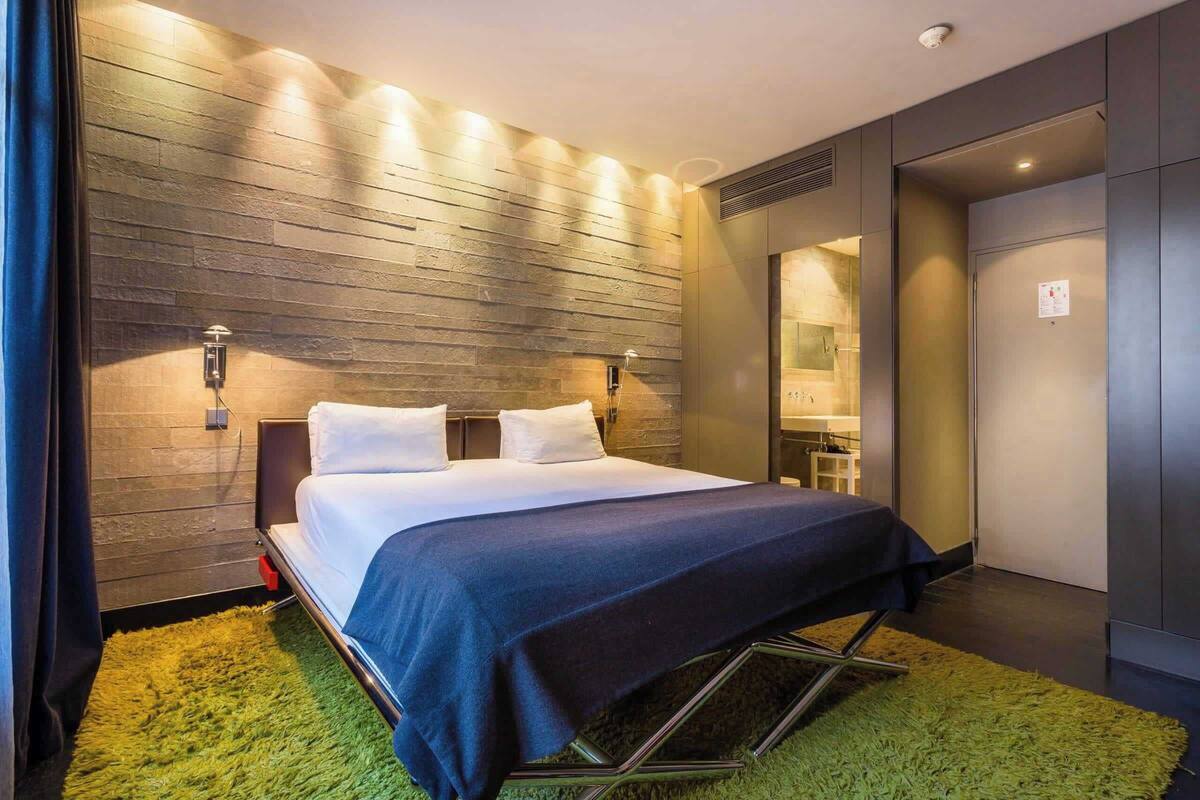 A modern hotel room with a bed, a green rug, and a wooden wall.