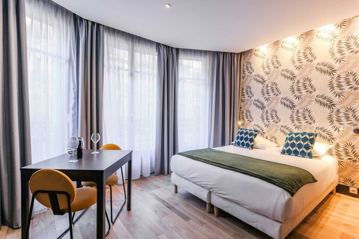 A bedroom with a bed, a table with chairs, and a window with curtains.