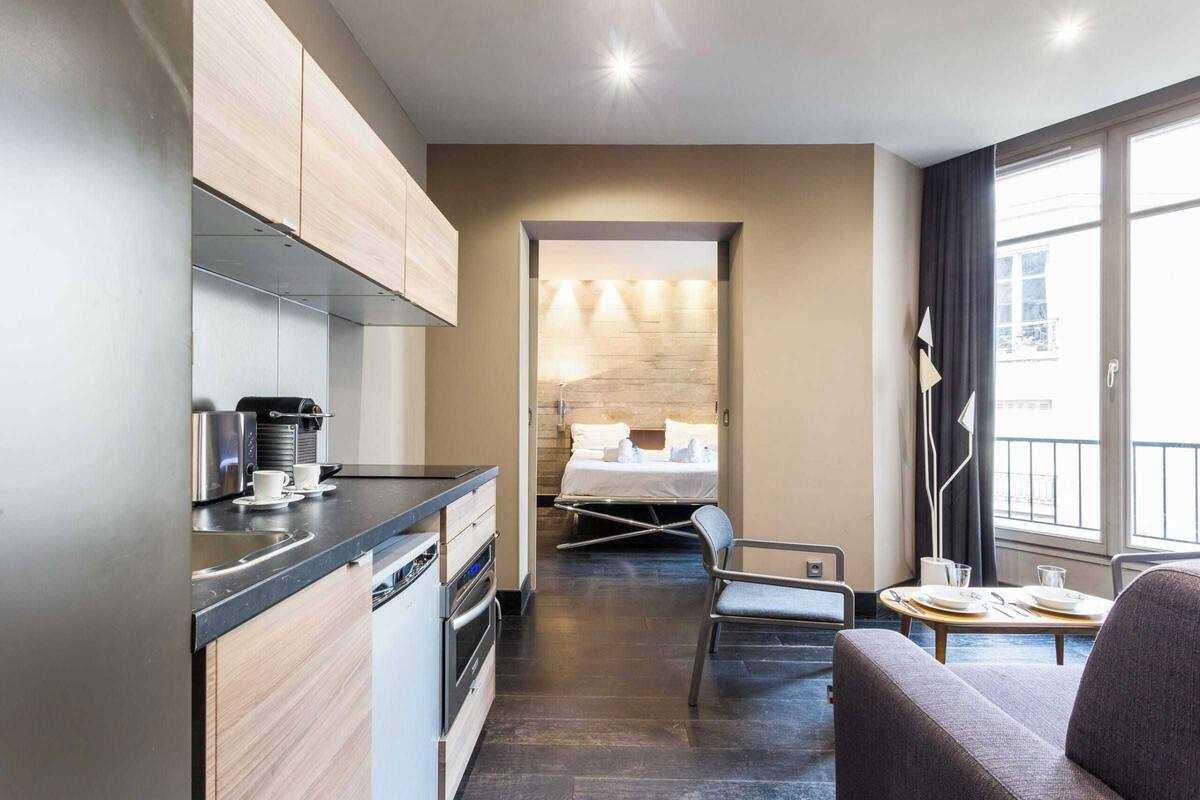 A modern hotel room with a kitchenette, a dining area, and a bed.