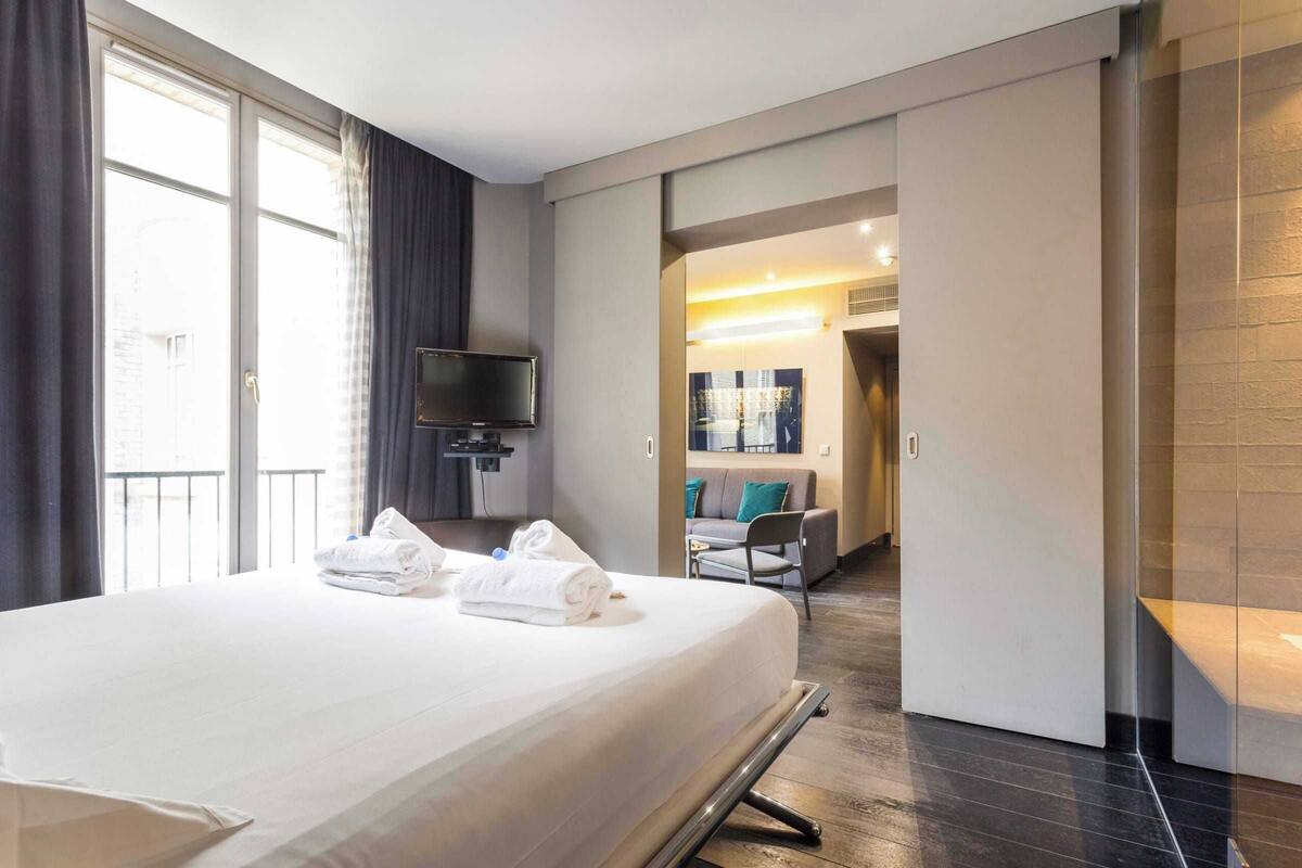 A hotel room with a large bed, a flat-screen TV mounted on the wall, and a sliding door leading to a balcony.