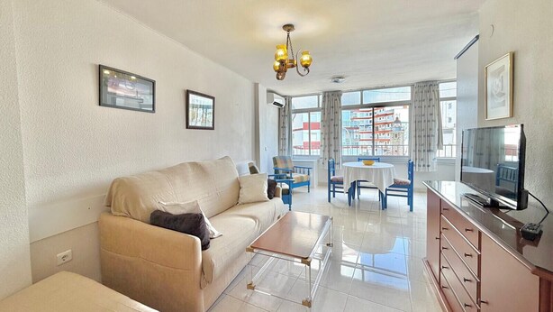 A living room with a sofa, coffee table, TV, and dining area with chairs and a table. - TERRASOL CARACOLA 2 (Torre del Mar)