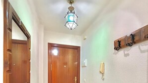 A hallway with a wooden door, a mirror, a small table with a vase, and a ceiling light fixture. - TERRASOL CARACOLA 2 (Torre del Mar)
