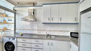 A modern kitchen with white cabinets, a built-in washing machine, and a microwave. - TERRASOL CARACOLA 2 (Torre del Mar)