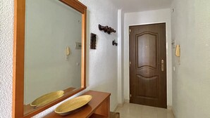 Un couloir avec une coiffeuse en bois, un grand miroir et une porte au fond.