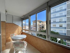 A balcony with a white table and chairs, large windows, and a view of a residential building. - TERRASOL CARACOLA 3 (Torre del Mar)