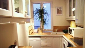 A compact kitchen with white cabinets, a dishwasher, a washing machine, and a microwave. - Appartement Entre la rue Mouffetard et le Jardin des Plantes (Paris)