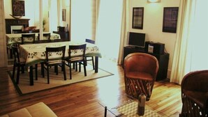 A dining area with a table set for four, a television on a stand, and a large mirror reflecting the room. - Appartement Entre la rue Mouffetard et le Jardin des Plantes (Paris)