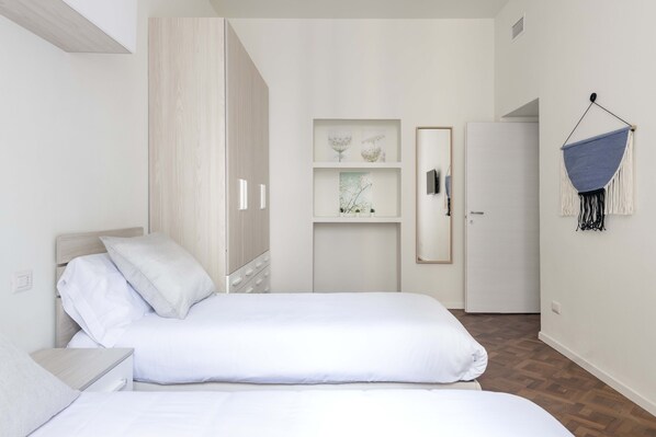 A bedroom with two beds, a wardrobe, a shelf with framed pictures, and a hanging chair.