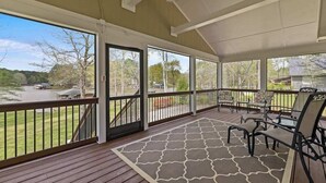 Eine überdachte Veranda mit Seeblick, Gartenmöbel und einem gemusterten Teppich.