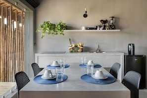 A modern kitchen with a dining area, featuring a central island with a sink, a built-in refrigerator, and a hanging plant. - Vila Flor Studios (Amontada)