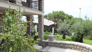 A stone-walled outdoor area with a curved pathway, a balcony with a black railing, and a large umbrella. - Villa Matilde - Paradiso Costiero, Fronte Mare, Terrazzo e Parcheggio Privato (Badesi)