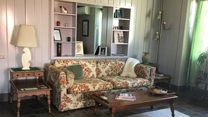 Un salon avec un canapé à motifs floraux, une table basse en bois et une bibliothèque.