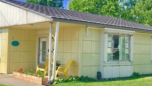 Un petit bâtiment d’un seul étage, doté d’un toit en tuiles et d’un porche. On y trouve une porte avec le numéro « 6 » et un panneau circulaire bleu sur le mur.