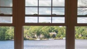 Ein Zimmer mit großem Fenster und Blick auf ein Gewässer sowie viel Grün.