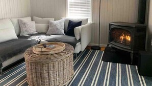 Ein gemütliches Wohnzimmer mit einer Couch, einem runden Korbsessel, einem Streifen Teppich, einer Stehlampe und einem Kaminofen.