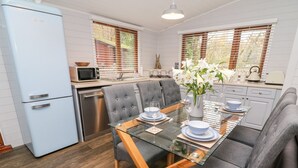 A modern kitchen with a blue refrigerator, grey upholstered chairs, a glass dining table, and a vase with white flowers. - Tree View Lodge (Windermere)