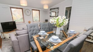 A modern dining area with a glass table, grey upholstered chairs, and a vase of white flowers. - Tree View Lodge (Windermere)