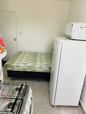 Een kleine, compacte kamer met een bed, een koelkast, een magnetron en een gasfornuis.