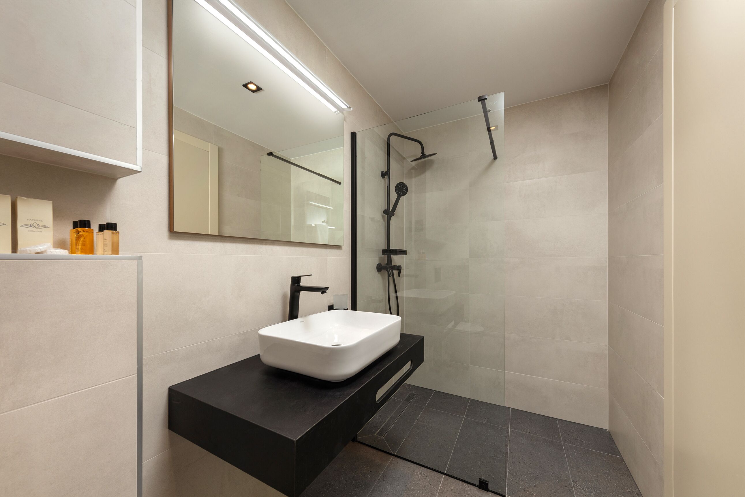 A modern bathroom with a white sink, black countertop, and a glass-enclosed shower area.