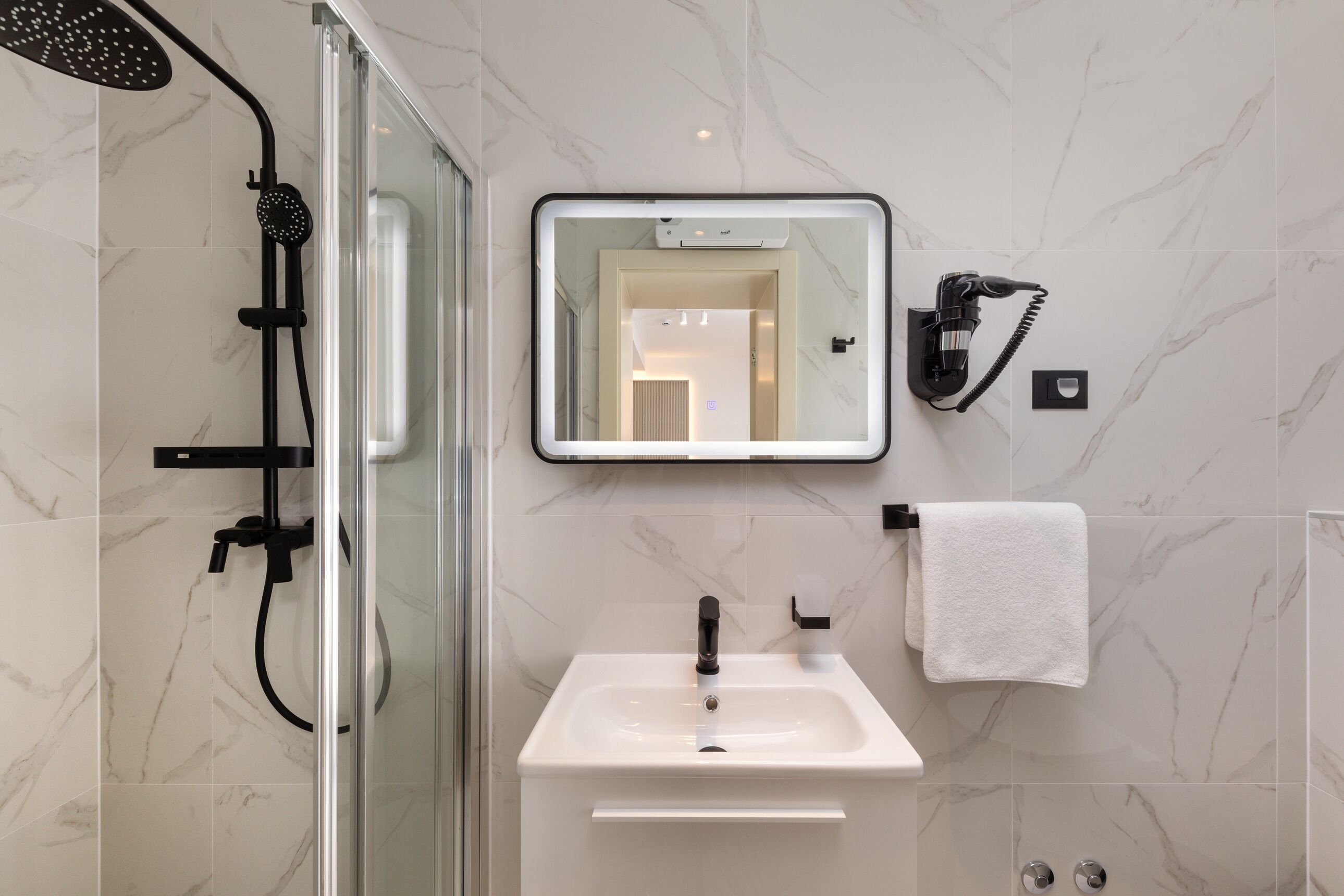 Une salle de bain moderne avec une douche à parois de verre, un lavabo blanc, un miroir et un porte-serviettes.