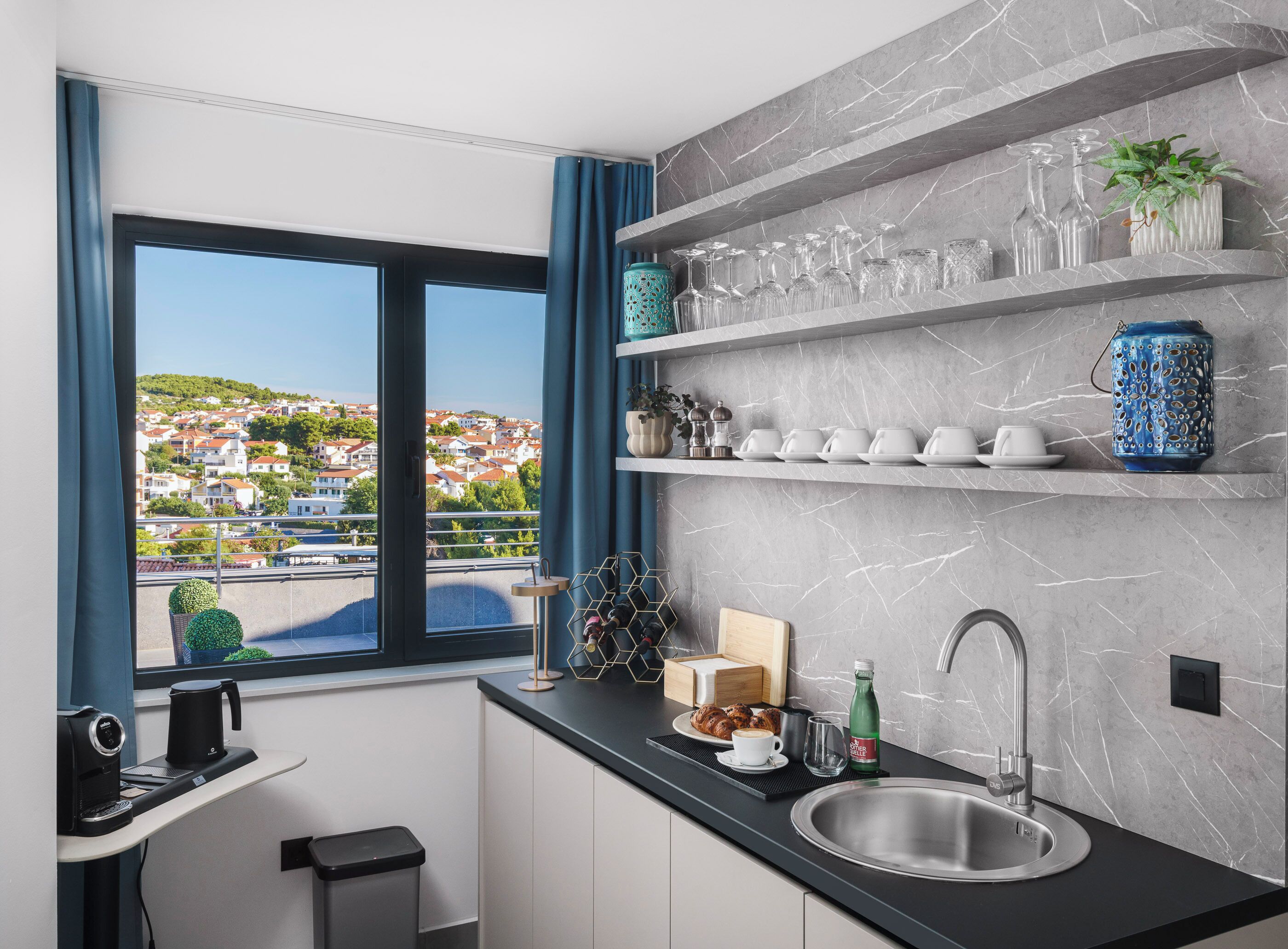 A modern kitchen with a view of a residential area, a coffee machine, a sink, and various kitchenware on shelves.