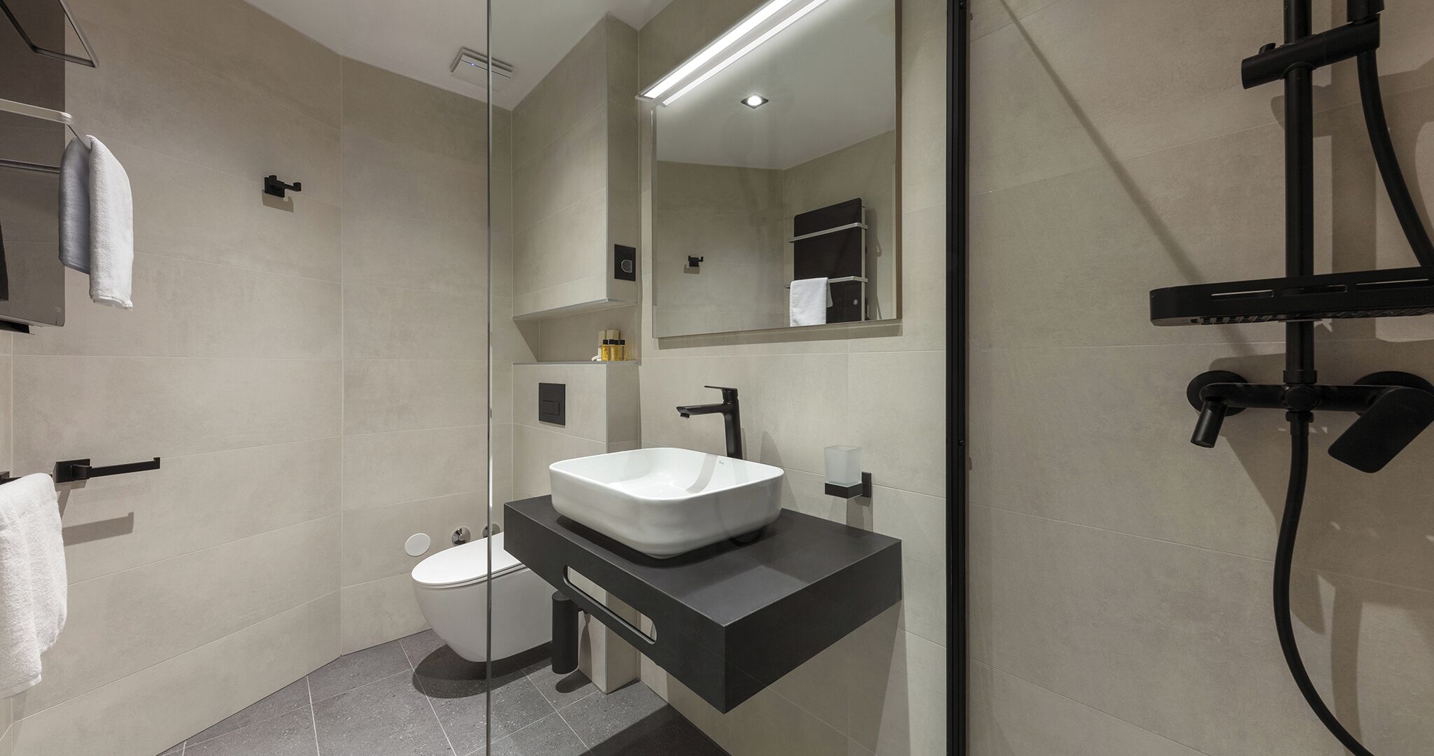 A modern bathroom with a white sink, black countertop, and a glass shower enclosure.