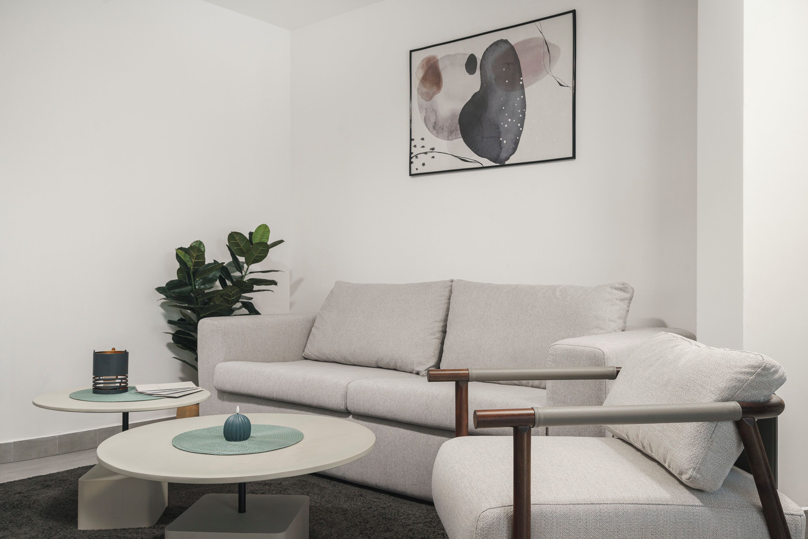 Una sala de estar moderna con un sofá gris, una mesa redonda de centro y una mesita auxiliar con una lámpara.