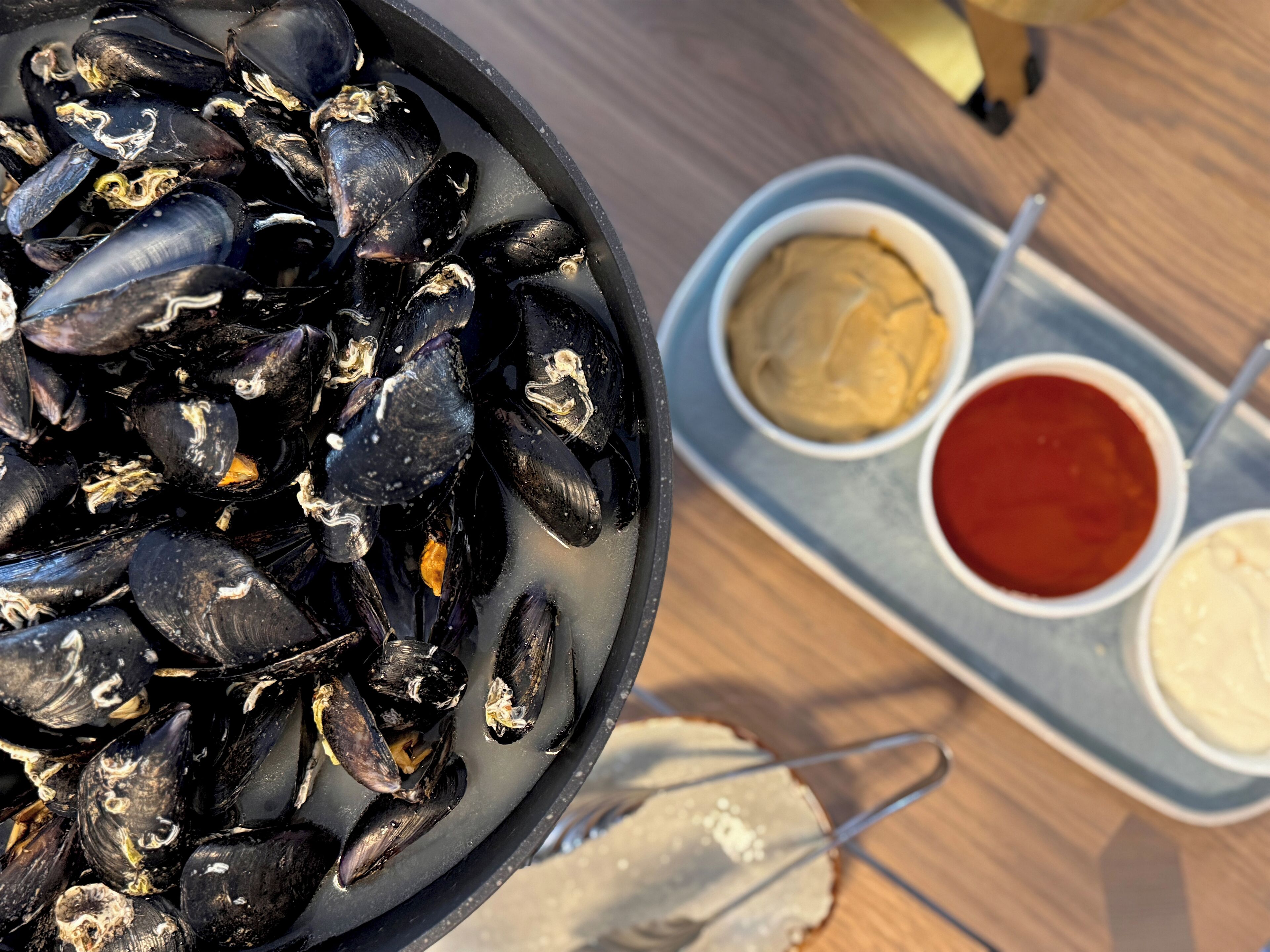 Un bol de moules, accompagné de deux petits récipients de sauce.