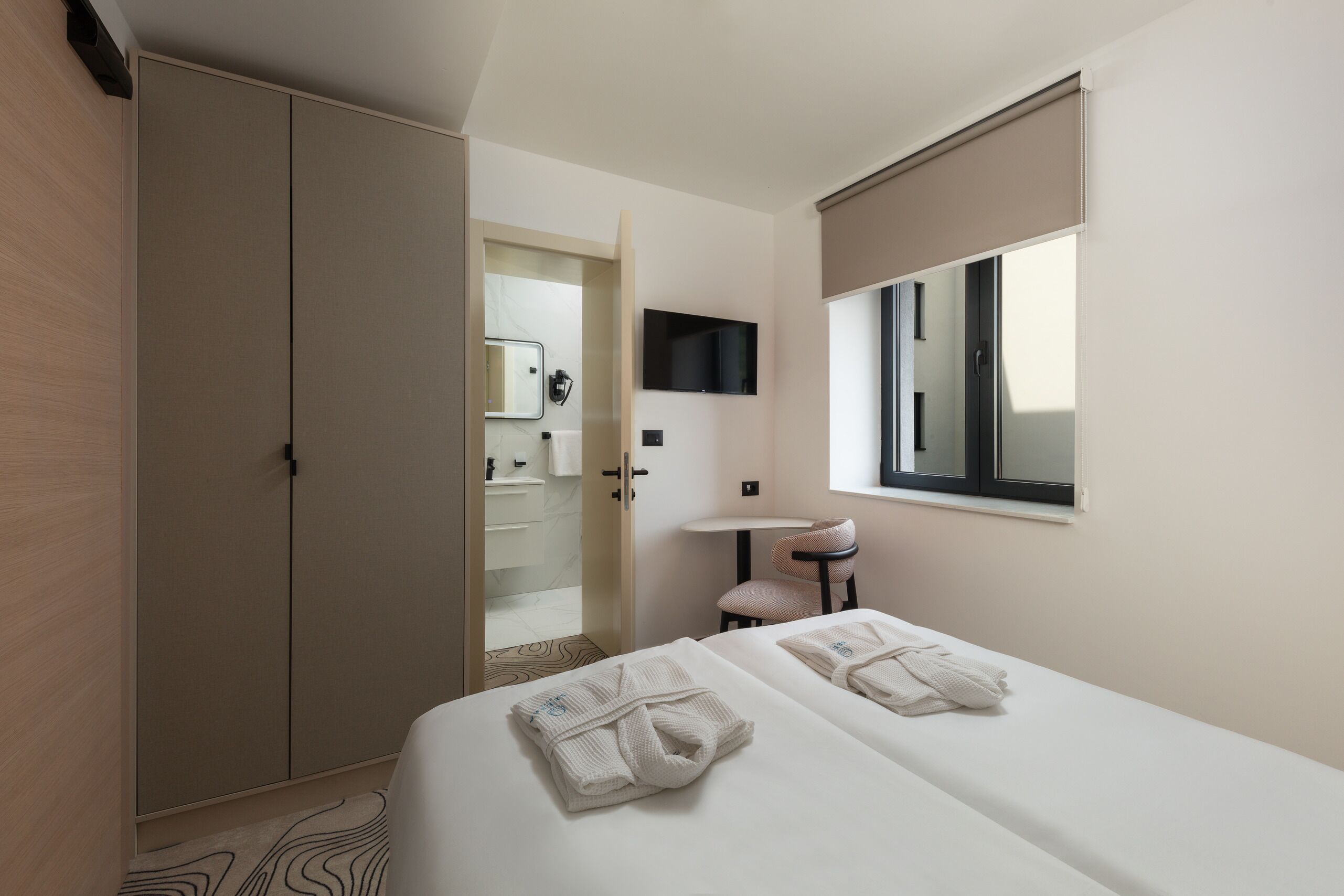 Ein Hotelzimmer mit Bett, zwei Handtüchern, Schreibtisch, Stuhl, Fernseher und Kleiderschrank.