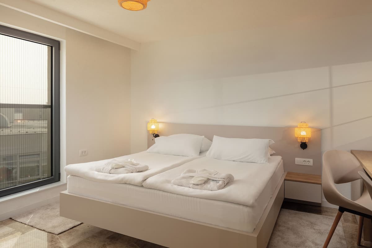 A hotel room with a large bed, two bedside tables, a chair, and a window with blinds.