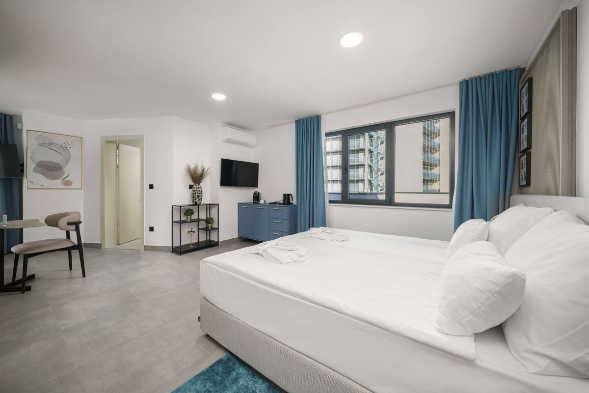 A modern bedroom with a large bed, a desk, a chair, and a TV.