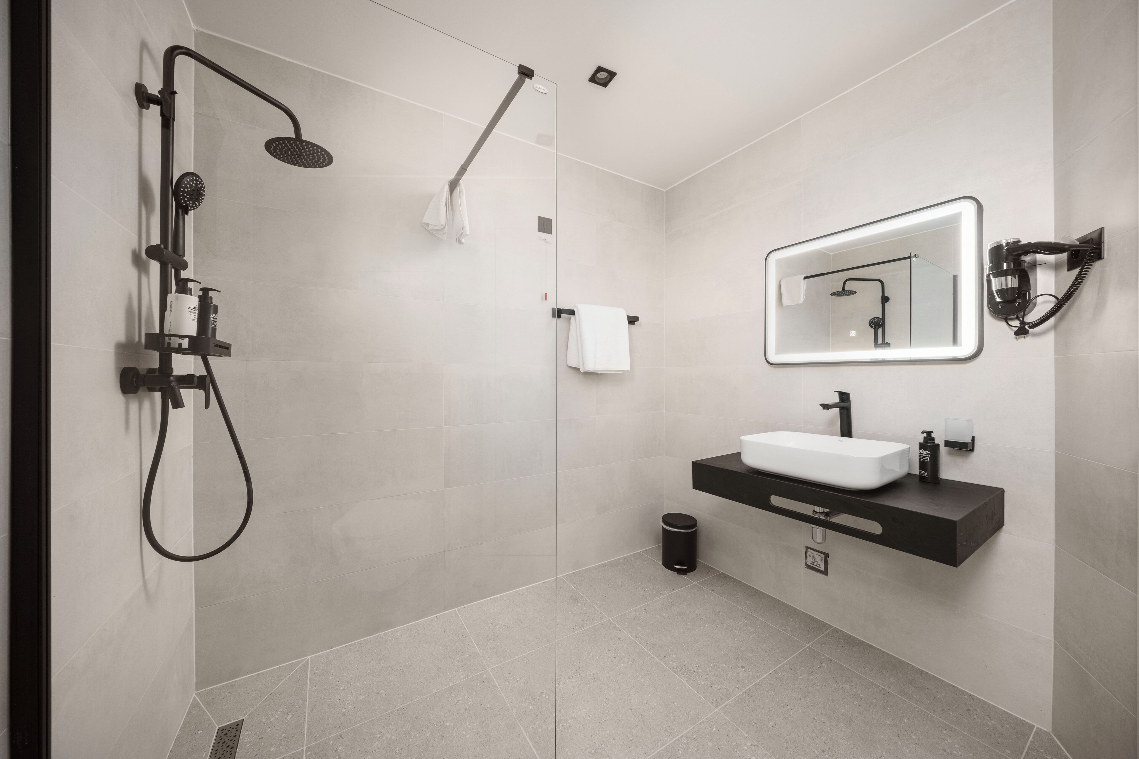 A modern bathroom with a glass-enclosed shower, a white sink, and a mirror with integrated lighting.