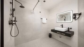 A modern bathroom with a glass-enclosed shower, a white sink, and a mirror with integrated lighting.
