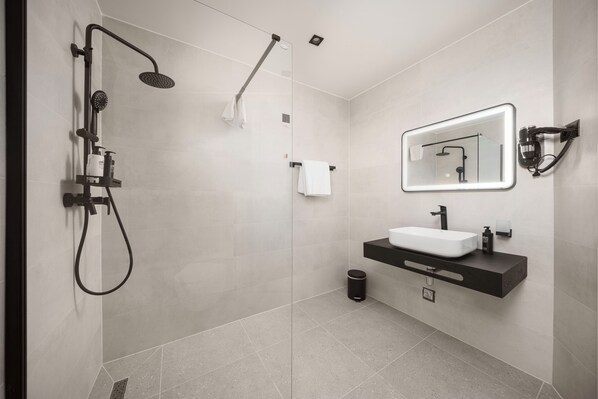 A modern bathroom with a glass-enclosed shower, a white sink, and a mirror with integrated lighting. - Seesea Hotel (Vodice)