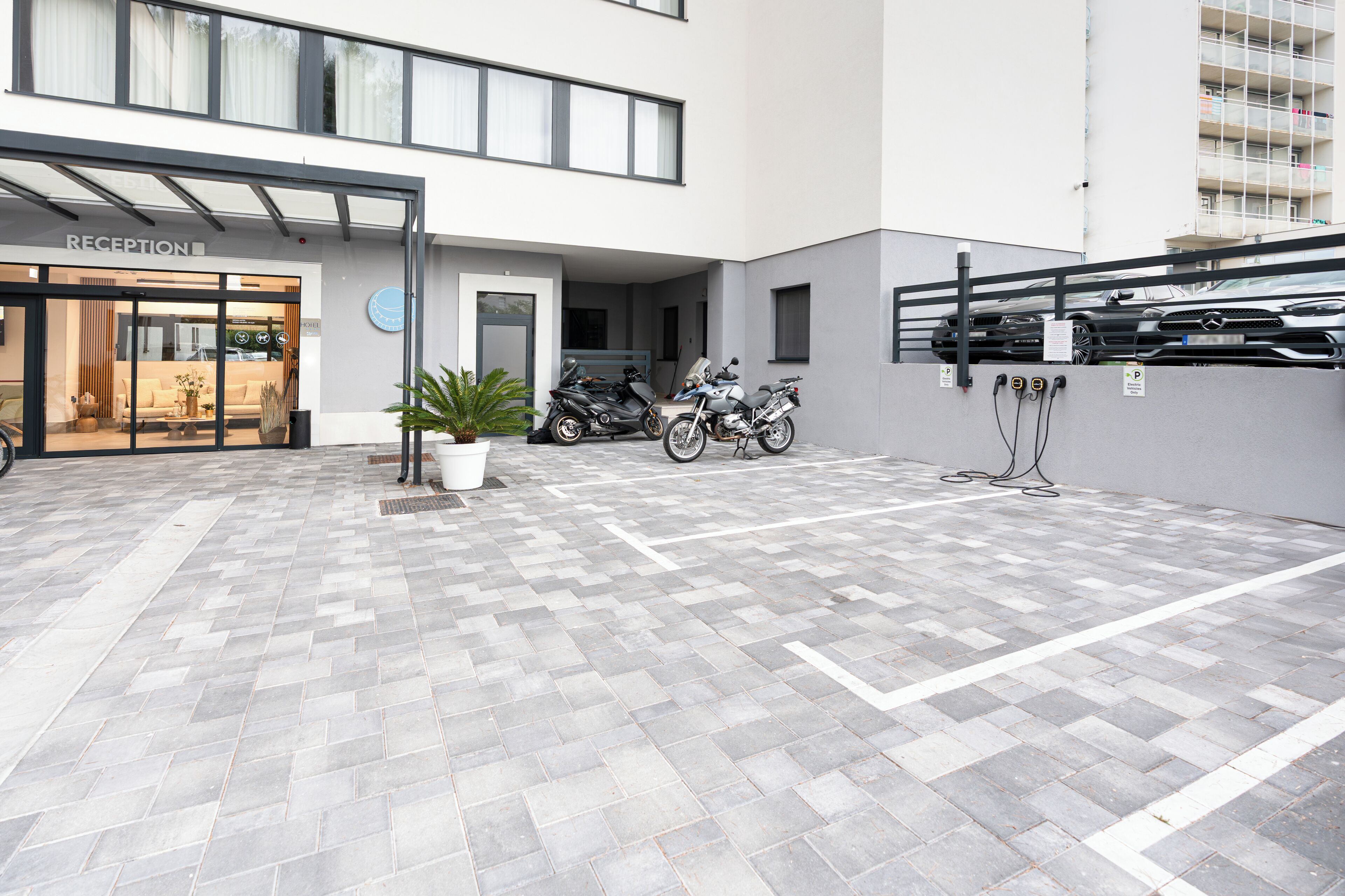 Un edificio moderno con una zona de recepción, dos motocicletas estacionadas afuera y un patio empedrado.