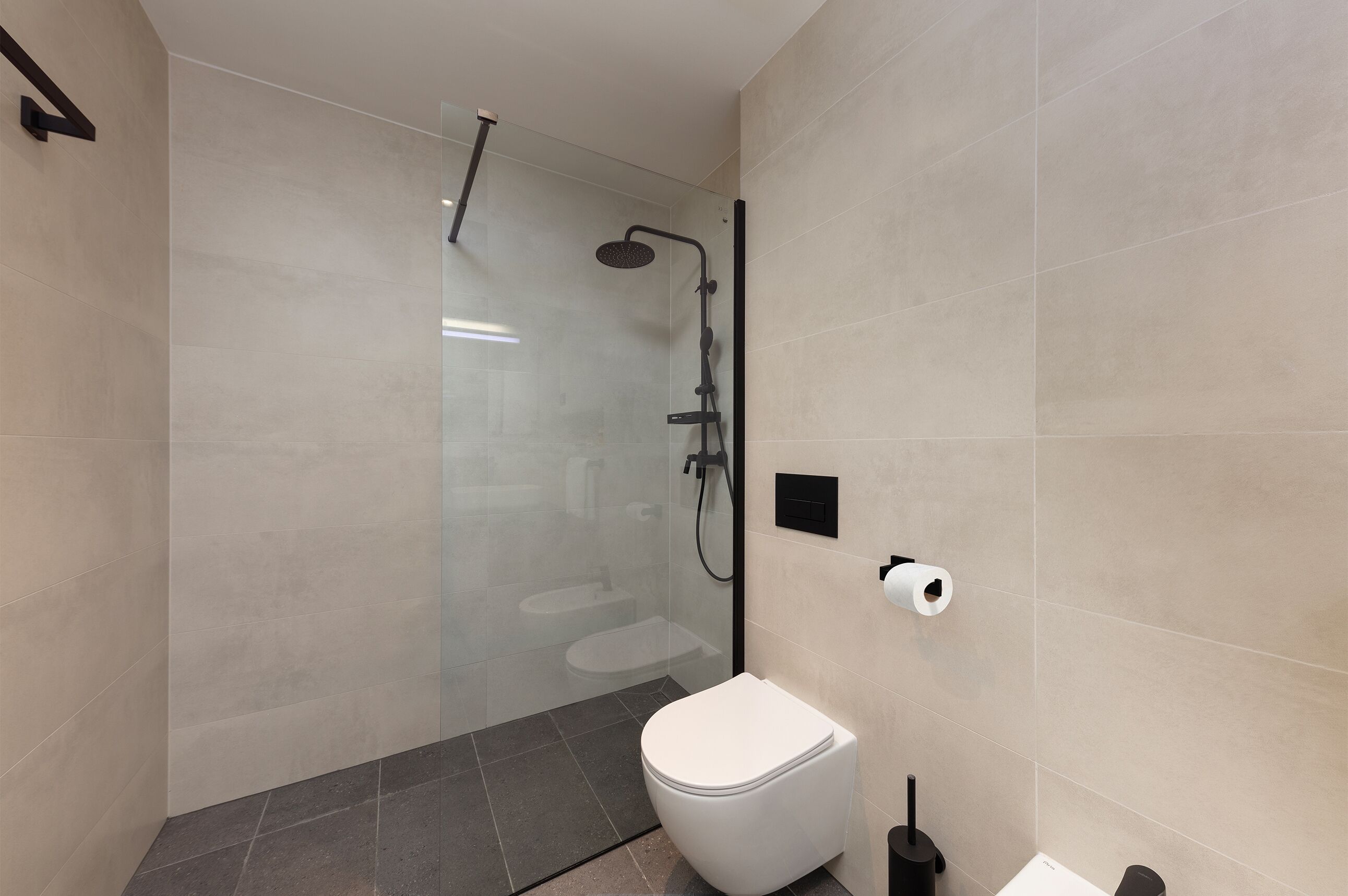 A modern bathroom with a glass-enclosed shower, a toilet, and a bidet.
