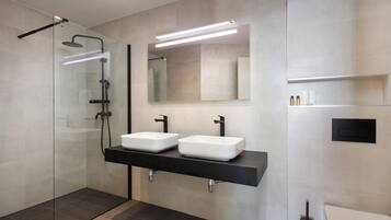 Ein modernes Badezimmer mit einer Duschkabine aus Glas, zwei weißen Waschbecken mit schwarzen Armaturen und einem großen Spiegel über den Waschbecken.