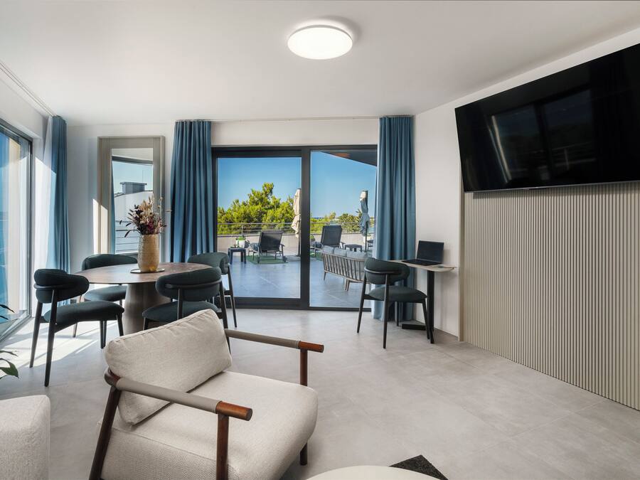 Quarto de hotel moderno com área de refeições, TV de tela plana e varanda com vista.