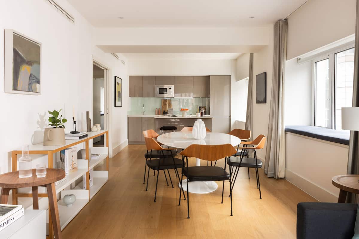 A modern kitchen with a central island, a dining area with a round table and chairs, and a view of the city through large windows.