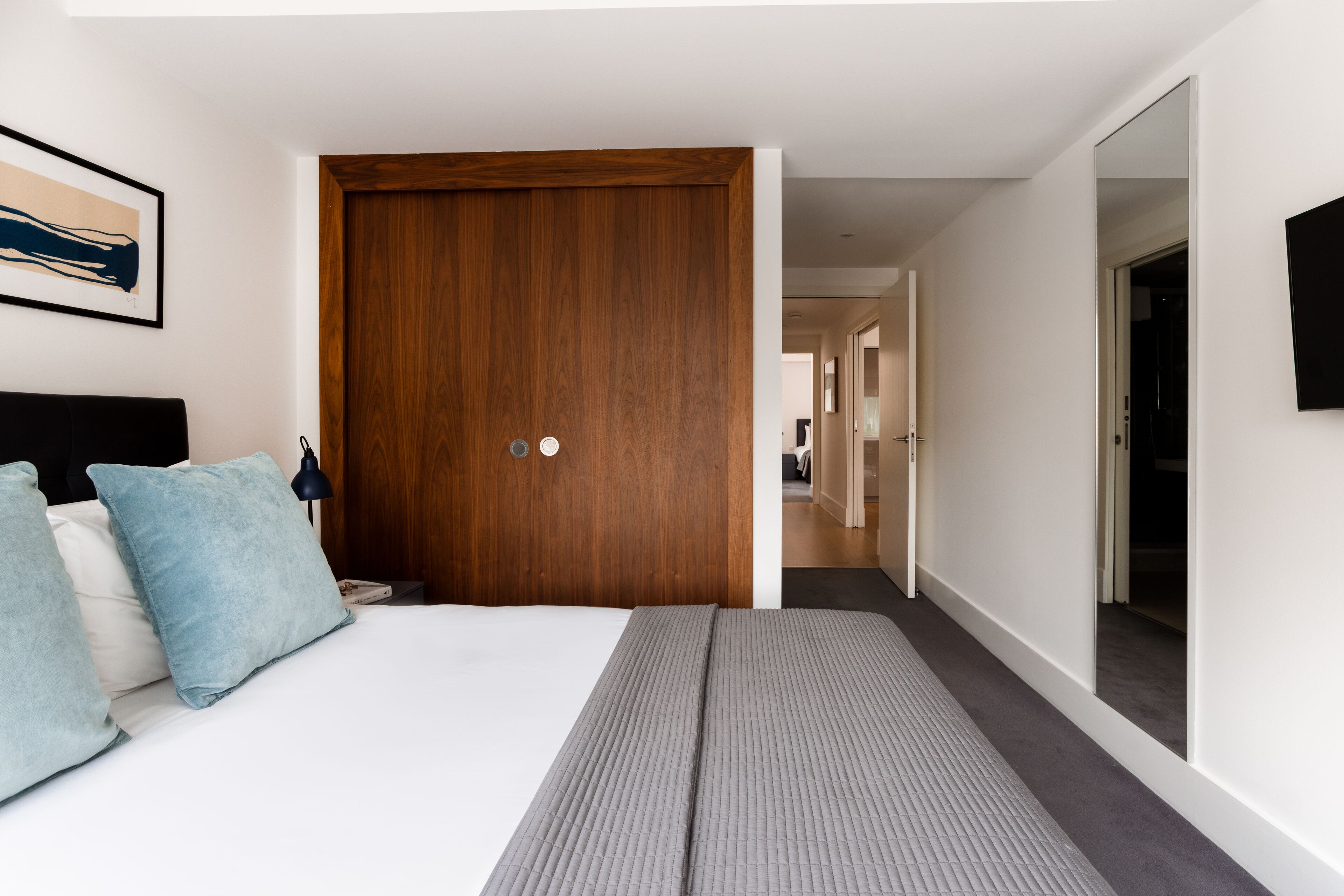 A modern hotel room with a large bed, a wooden door, and a hallway leading to other rooms.