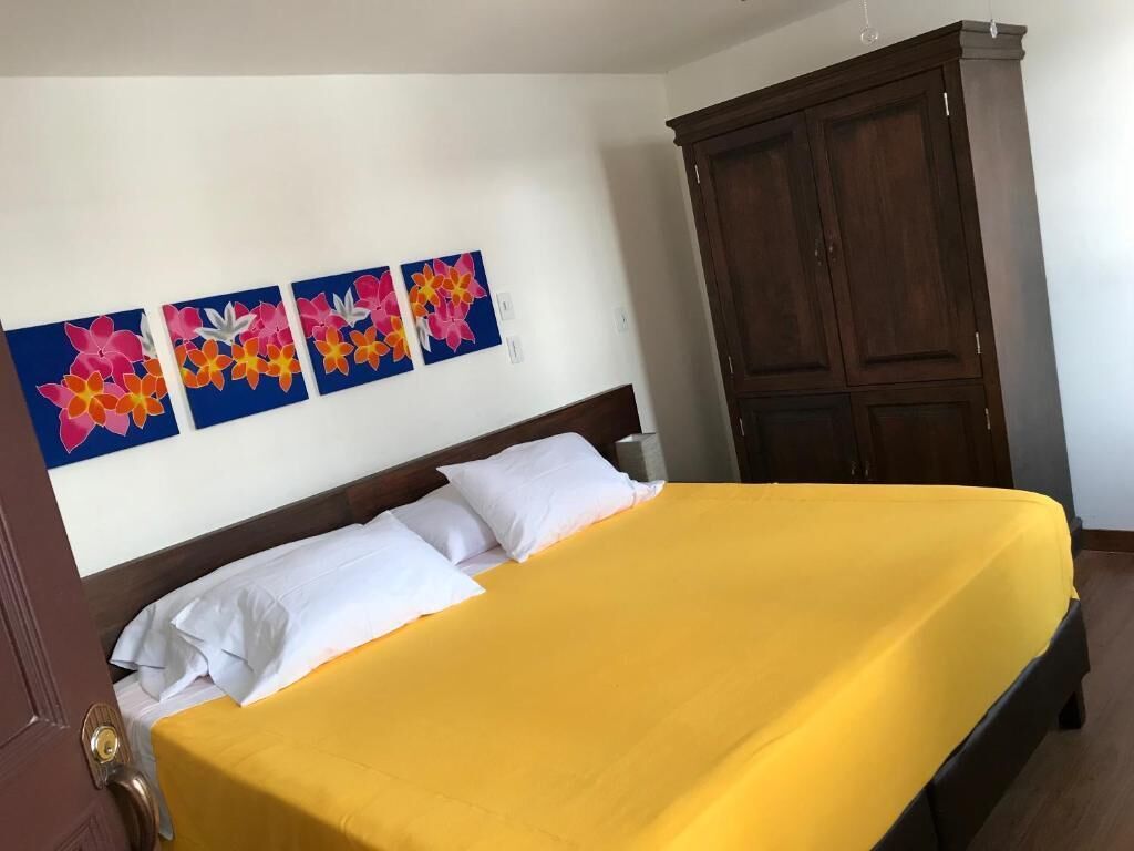 Una camera d'albergo con un letto, cuscini bianchi, una coperta gialla e un armadio in legno.