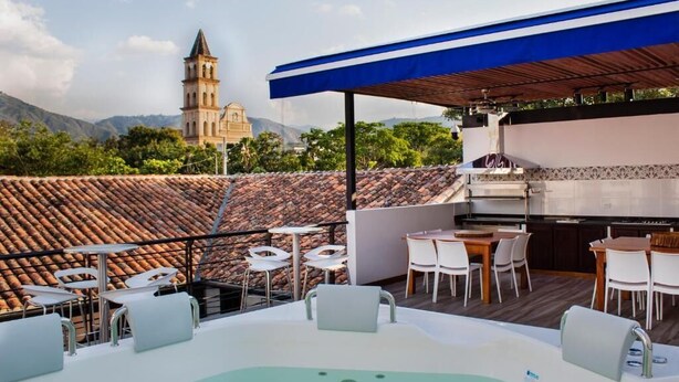 Terraza en la azotea con jacuzzi, mobiliario exterior, una parrilla y vistas a una iglesia y montañas.
