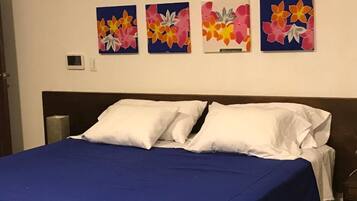 Una cama con almohadas blancas y una colcha azul, flanqueada por cuatro cuadros florales en la pared.