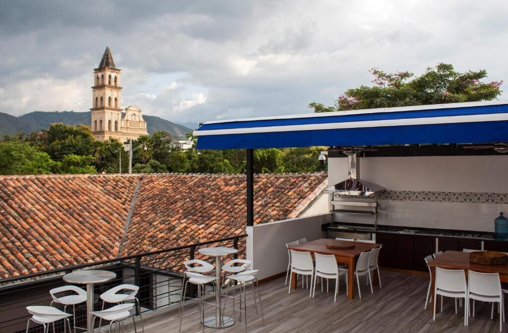 Um terraço no telhado com área de churrasqueira, cadeiras brancas e vista para uma torre histórica.