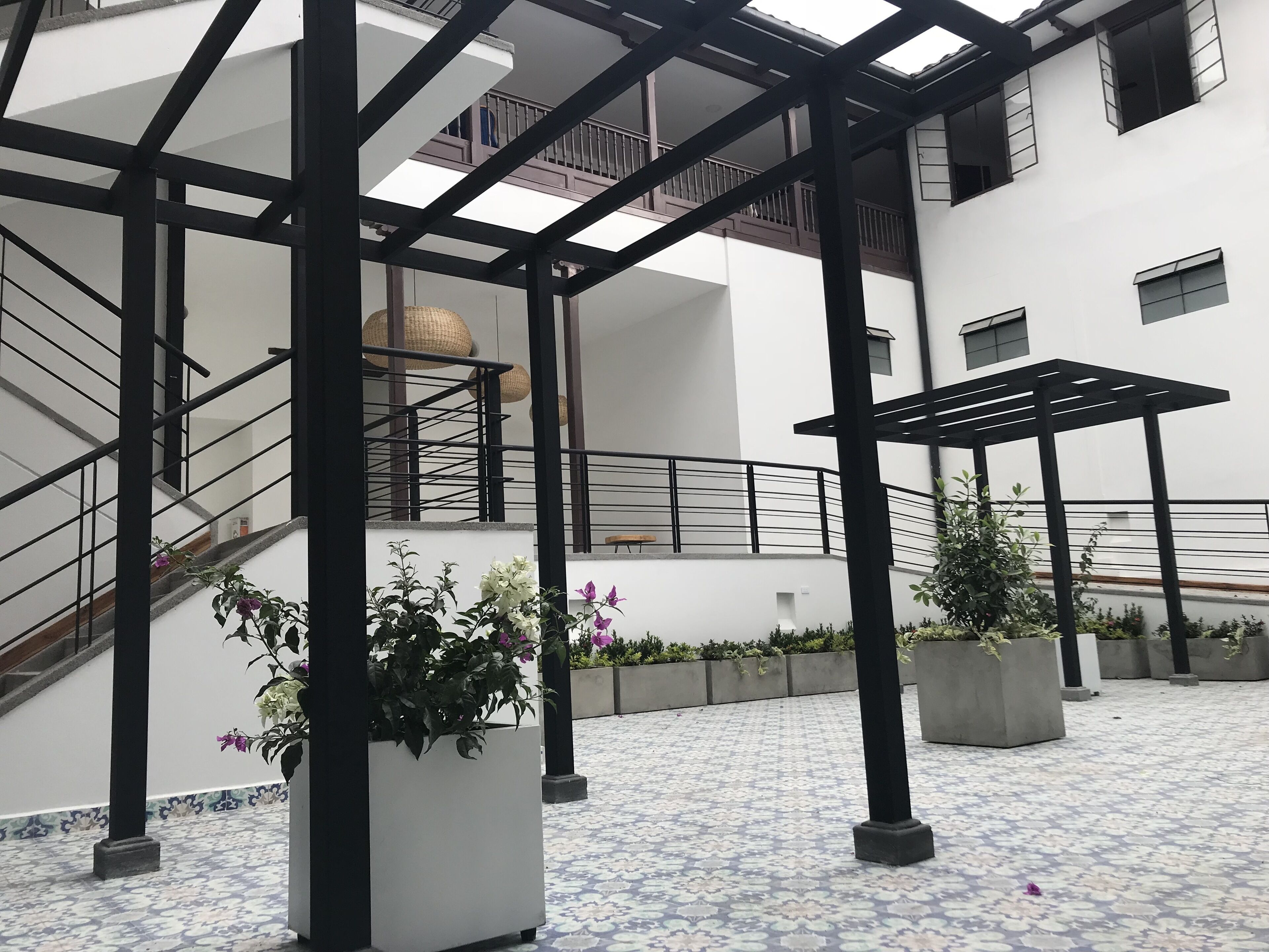 A modern building with a covered outdoor area featuring a tiled floor, black metal railings, and potted plants.