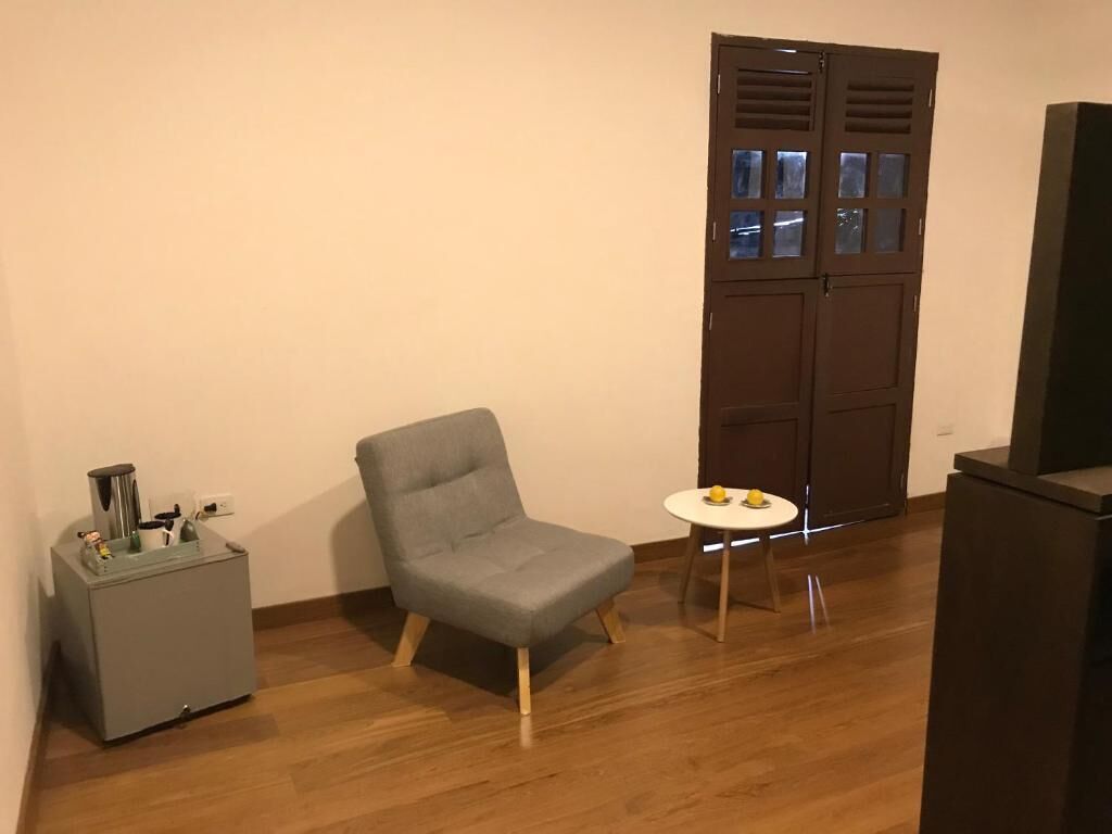 A small room with a grey armchair, a small table with two lemons, a grey cabinet, and a wooden door with glass panels.