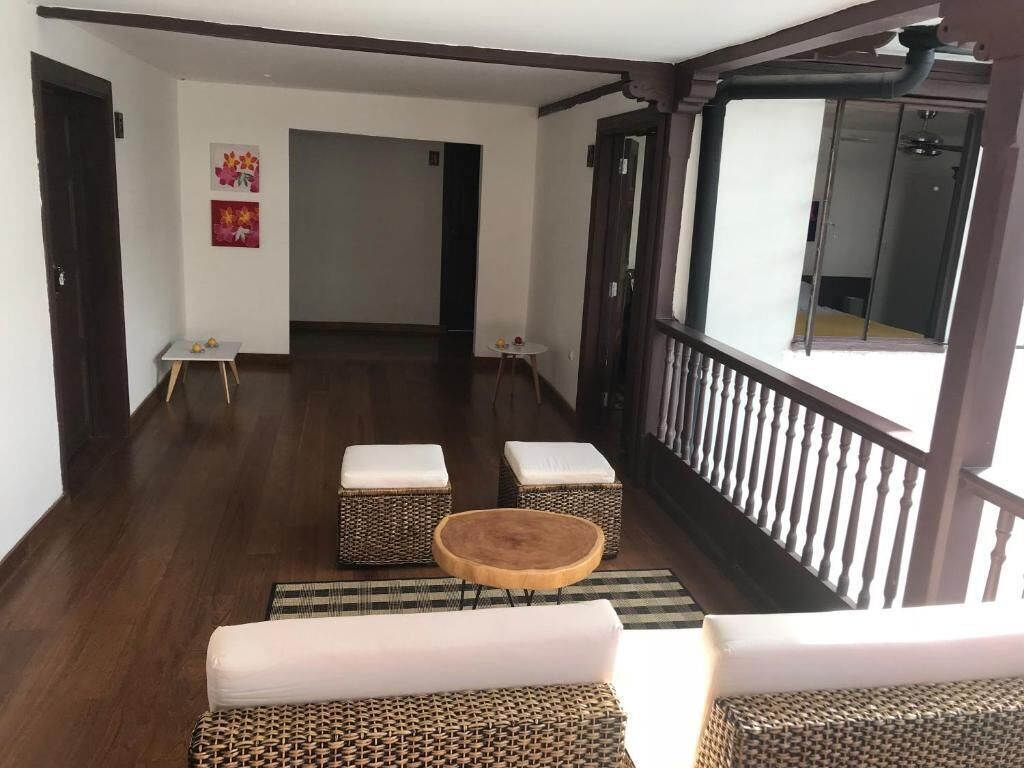 Una habitación amplia con piso de madera, un balcón con barandilla y mobiliario de mimbre.